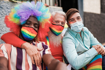 Gay multiracial men at lgbt gay pride event taking a selfie together while wearing protective face mask for coronavirus - Young and senior men