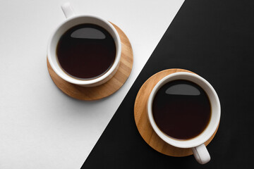 Two coffee cups on wooden saucers against black and white diagonally divided background. Tea together concept