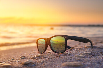 Fototapeta na wymiar Sunglasses lie in the sand on the sea coast at sunset. Holidays and vacations by the ocean