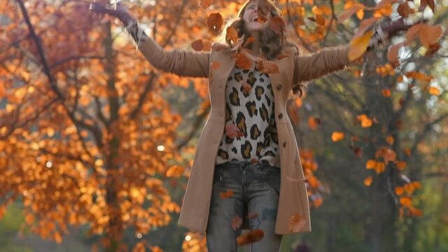 Hello november. smiling trendy 40 years old woman in beige coat and orange hat rejoicing outside in the city park in autumn. 