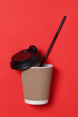 Takeaway paper cup, black caps and drinking straw lie on red background.