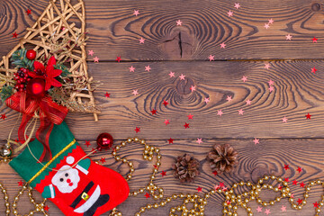 Red felt stocking with the image of Santa, a golden ratang bell with Christmas decorations, pine cones, snowflakes, shiny beads on a wooden table. Top view, copy space.