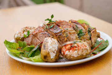 Defocused blurred baked meat with potatoes decorated with spices and herbs on a white plate close-up.
