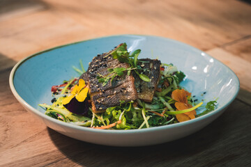 Pan fried sea bass fillets served on a bed of Asian vegetable salad, garnished with micro herbs, viola flowers and sesame seeds.