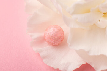 Delicate close-up shot of pink ball of pearl face powder on petals of carnation flower. Concept for articles on makeup.