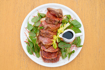 Rare meat steak with spices and sauce garnished with greens.