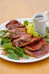 Rare meat steak with spices and sauce garnished with greens side view.