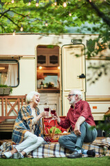 Naklejka premium Happy elderly man and woman talking while having picnic near camper van