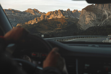 Men's hands hold the steering wheel. For Konami view of the mountain pass. Dolomites, Italy.