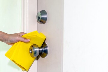 Cleaning door knob, hand using yellow all-purpose cloth cleaning and polishing surface of the door knob for disinfect virus bacteria, prevent from epidemic of disease during the corona virus outbreak.