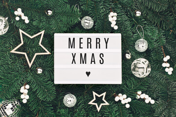 Fototapeta na wymiar Merry Xmas text on white Lightbox with holiday silver and white decorations, acorns on Christmas tree branches background.