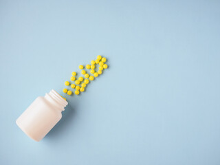 Minimalism style template for medical blog. White medicine bottle and small round yellow pills spilled out blue paper background. Pharmaceutical and health care concept. Medicine pills. Flat lay