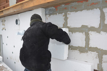 A building contractor is installing an external solid wall insulation fixing insulating polystyrene...