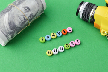 Selective focus of banknote, toy camera and alphabet beads with text TRAVEL BUDGET on a green background.