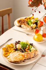 Delicious hearty dinner in plates on the table, fried pork entrecote on the bone with stewed pumpkin pieces and salad, green salad with cauliflower and napa cabbage, bell pepper and spices