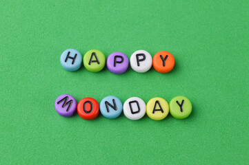 Top view of colorful alphabet beads with text HAPPY MONDAY on a green background.