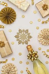 Festive background with gold decoration , gift boxes with bottle of sparkling wine, shiny golden serpentine confetti and paper christmas tree decorations, glittering snowflakes