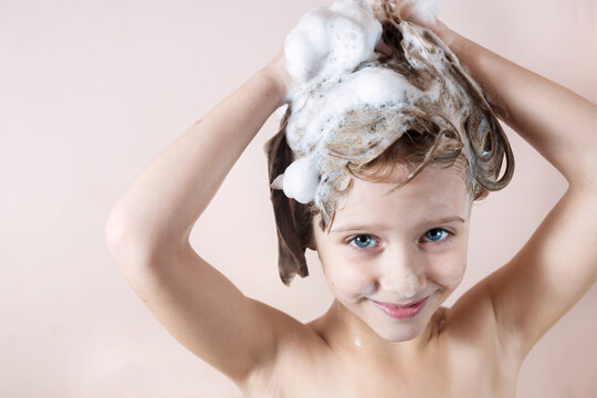adorable little girl with blue eyes washing her hair in the bathroom and laughs, foam on the head, look at the camera