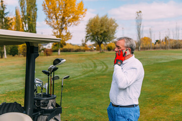 Senior golfer talking on the smartphone while playing golf in autumn