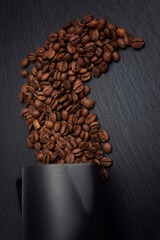 Scattered grains of roasted coffee on a black textured background. Top view. Vertical.