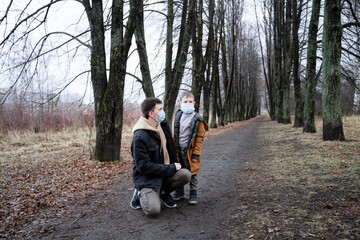 father and son look into the distance in medical masks, walk in the winter park, autumn forest, against the background of dry trees, pandemic time, for security reasons, sad dad and son, modern societ