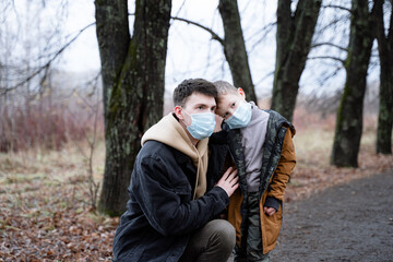 father and son look into the distance in medical masks, against the background of dry trees, pandemic time, for security reasons, sad dad and son, modern society, father and son portrait