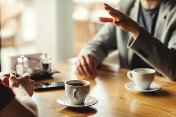 Closeup hands of two unrecognizable male business partners having business talk over espresso coffee sitting at table in cafe