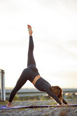 athletic caucasian woman doing exercises on mat outdoors on fresh air in the morning, strethcing alone, wearing sportive outfit, do one-legged downward-facing dog pose