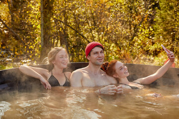 young cheerful caucasian friends in the traditional japanese bath ofuro, barrel-furako. they relax,...