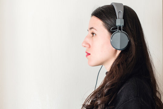 Una mujer joven morena de perfil escuchando m&uacute;sica con unos auriculares grises