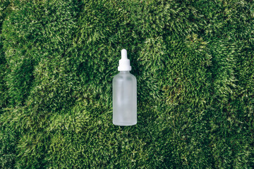Transparent glass bottle with serum, essential oil, cosmetic product on green grass, moss background. Top view. Natural organic, spa cosmetic concept. Biophilia design. Alternative beauty treatment