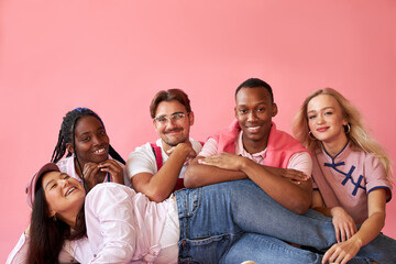 excited interracial group of youth have fun, smile, laugh, isolated onver pink background, they are enjoying time together