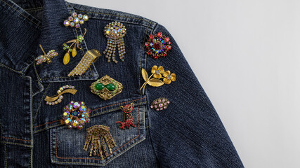 A variety of beautiful multi colored vintage brooches are  pinned on a dark blue denim jacket. Amazing  and rare jewelry from the past that needs to be protected.  - obrazy, fototapety, plakaty