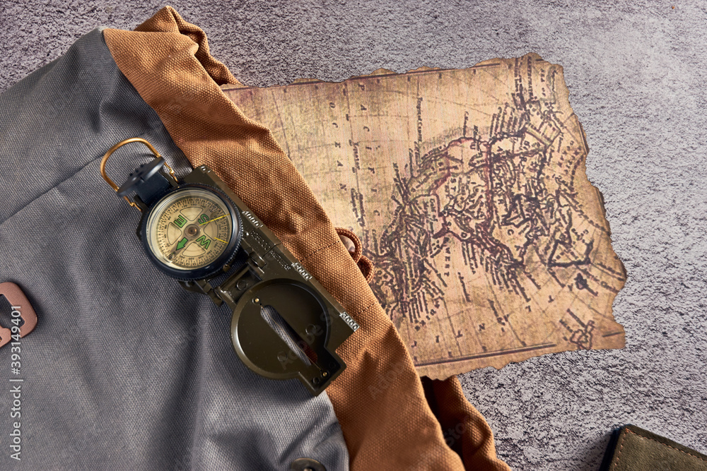 Poster top view closeup of a compass placed on a colorful fabric next to an ancient map