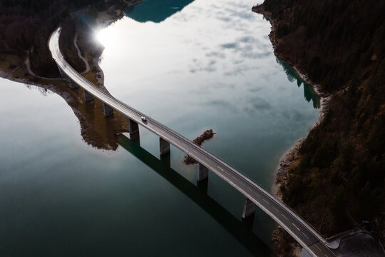Drone view of car driving along suspension bridge over calm river in autumn