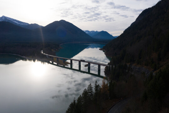 Drone view of car driving along suspension bridge over calm river in autumn