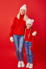 Fototapeta premium mother and daughter in warm clothes ready for winter, posing at camera, full-length portrait, isolated on red studio background