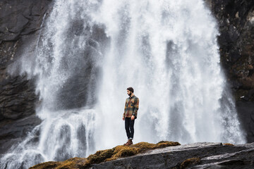 Male hiker standing on hill near waterfall in highland area in winter