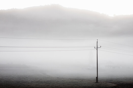 Minimalist gray scenery with electric pole and cables in misty mountain valley in cold morning
