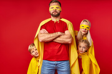 super family in hero cloaks standing isolated on red studio background, brave parent with members of family