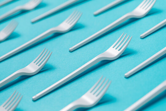 Top view flat lay composition of disposable white plastic forks for takeaway food arranged on blue background