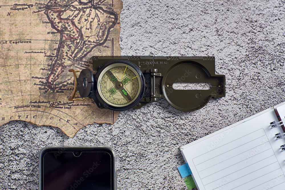 Poster top view closeup of a compass placed on an ancient map next to a notebook and a phone