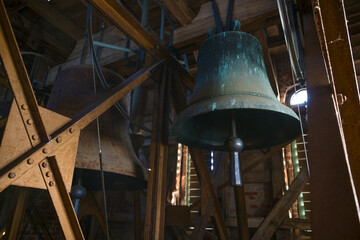 Fototapeta premium Heavy bells hanging in a metal frame in the tower of the city church of Gadebusch, they chime at worships and Christian holidays like Christmas and Easter