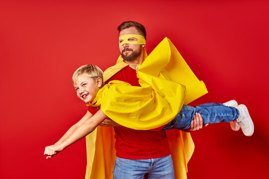 dad and kid boy play superhero game, imitate flight isolated over red studio background, dream to be superhero, entertainment