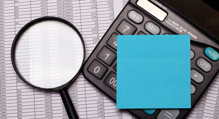 Calculator with blue sticker for notes, magnifier and reports on the desktop. Copy space