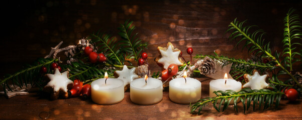 Four lighted small candles for the fourth Advent with Christmas decoration on dark rustic wood,...