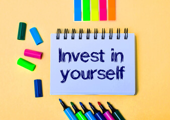 On a beige background, a notebook with the word INVEST IN YOURSELF, bright felt-tip pens and stickers