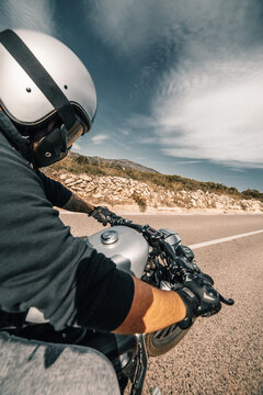 Back view cropped unrecognizable male rider in leather jacket and helmet riding motorbike on roadside against cloudy sky in countryside