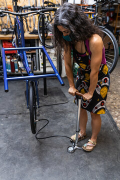 Full length of adult ethnic female mechanic inflating bicycle tire with pump while working in professional workshop