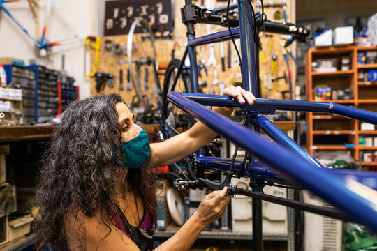 Side view of female worker in protective mask installing break and transmission wires on bicycle during maintenance service in workshop